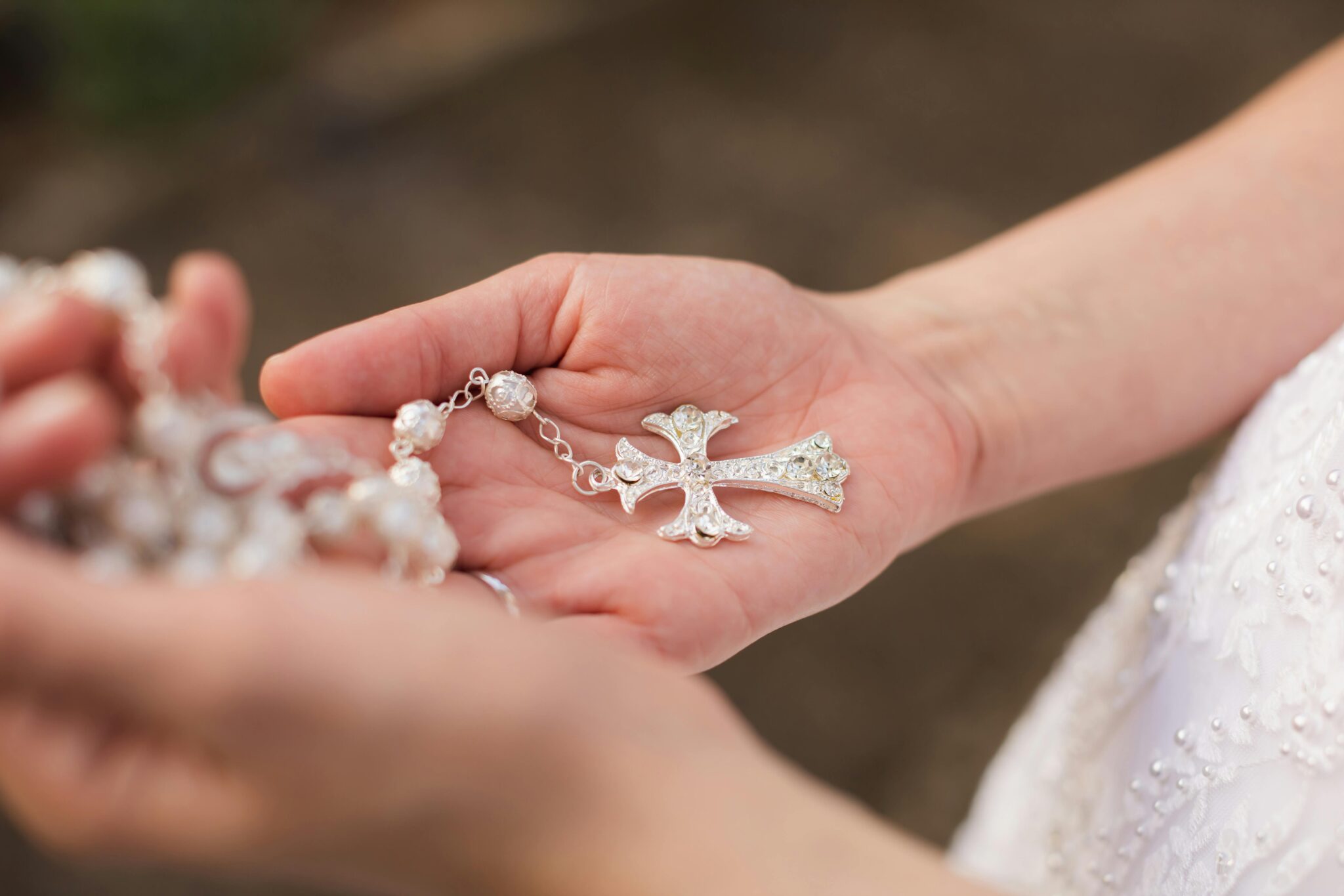 Close-up of a bride's hand holding a cross necklace, symbolizing faith and love.
