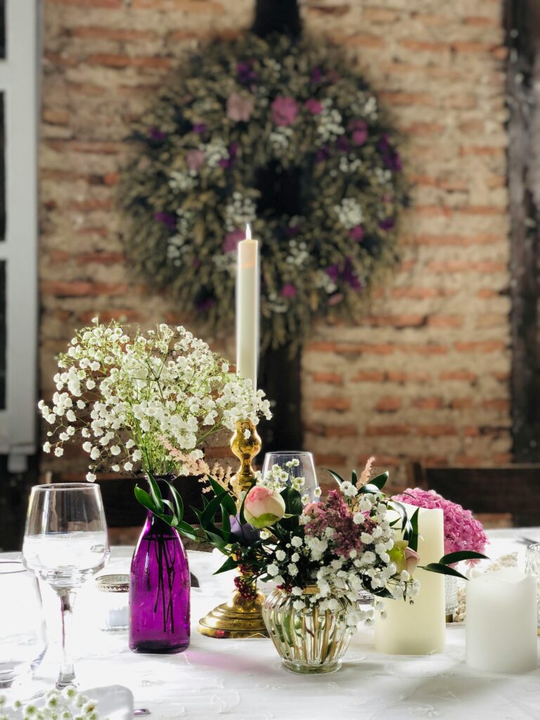 Charming table setup featuring vibrant flowers, candles, and rustic decor against a brick wall.