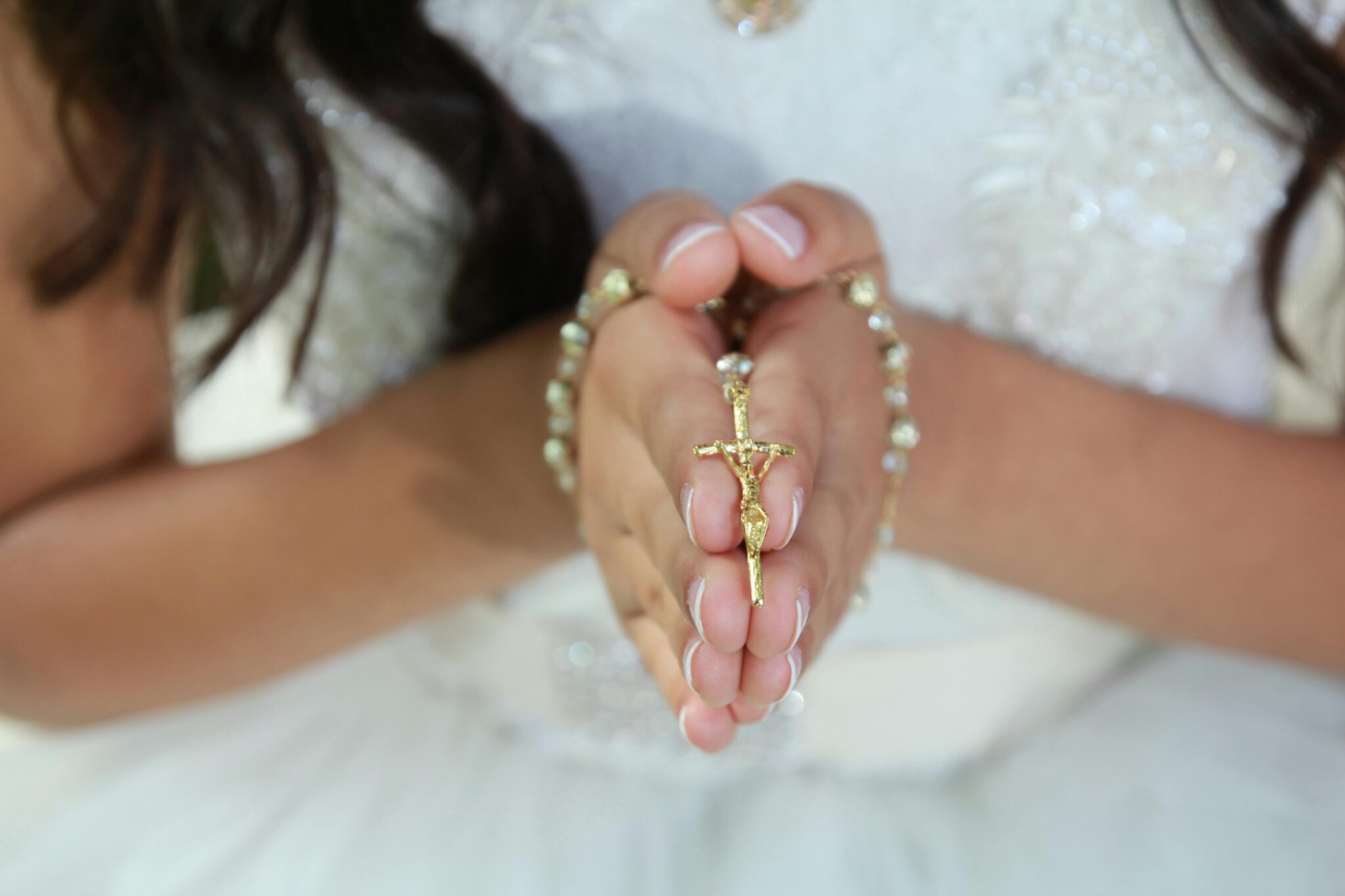 Close-up of a child's hands clasping a rosary, symbolizing faith and spirituality.