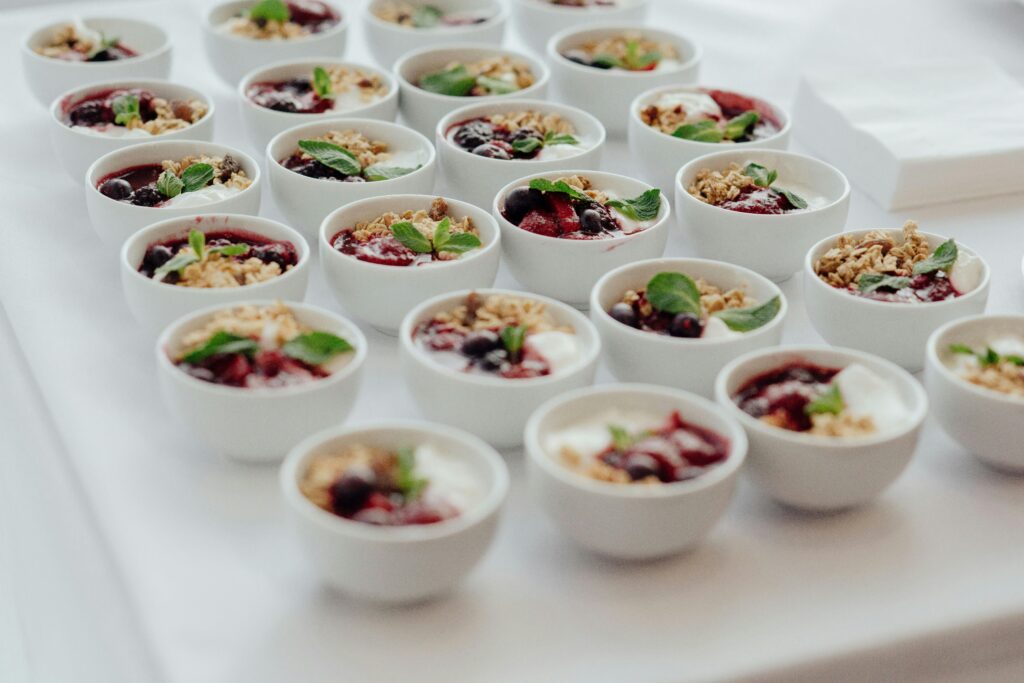 White bowls of delicious granola with berries served with yogurt and topped with mint leaves placed on table in cafe during breakfast